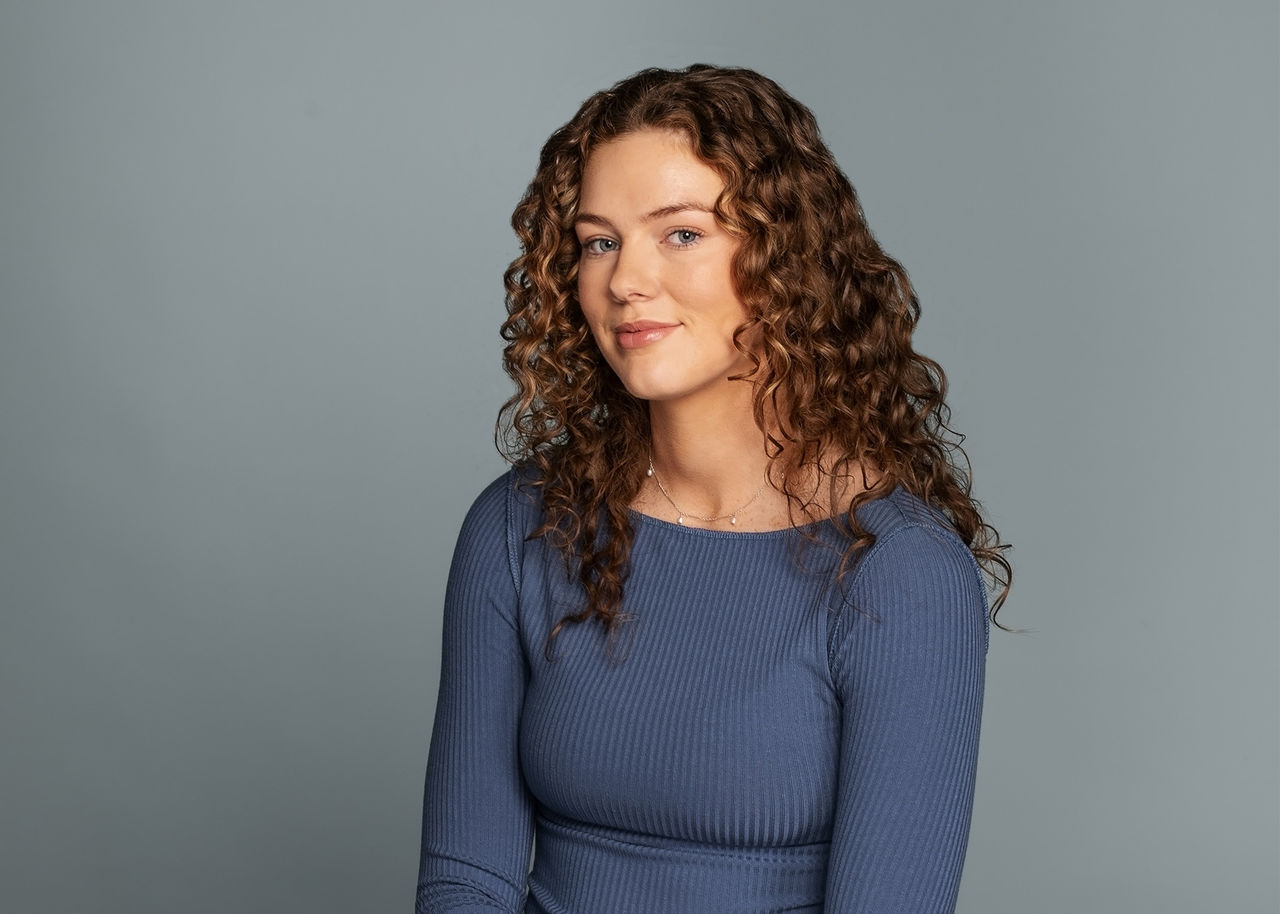 Female student with blue sweater in front of blue wall
